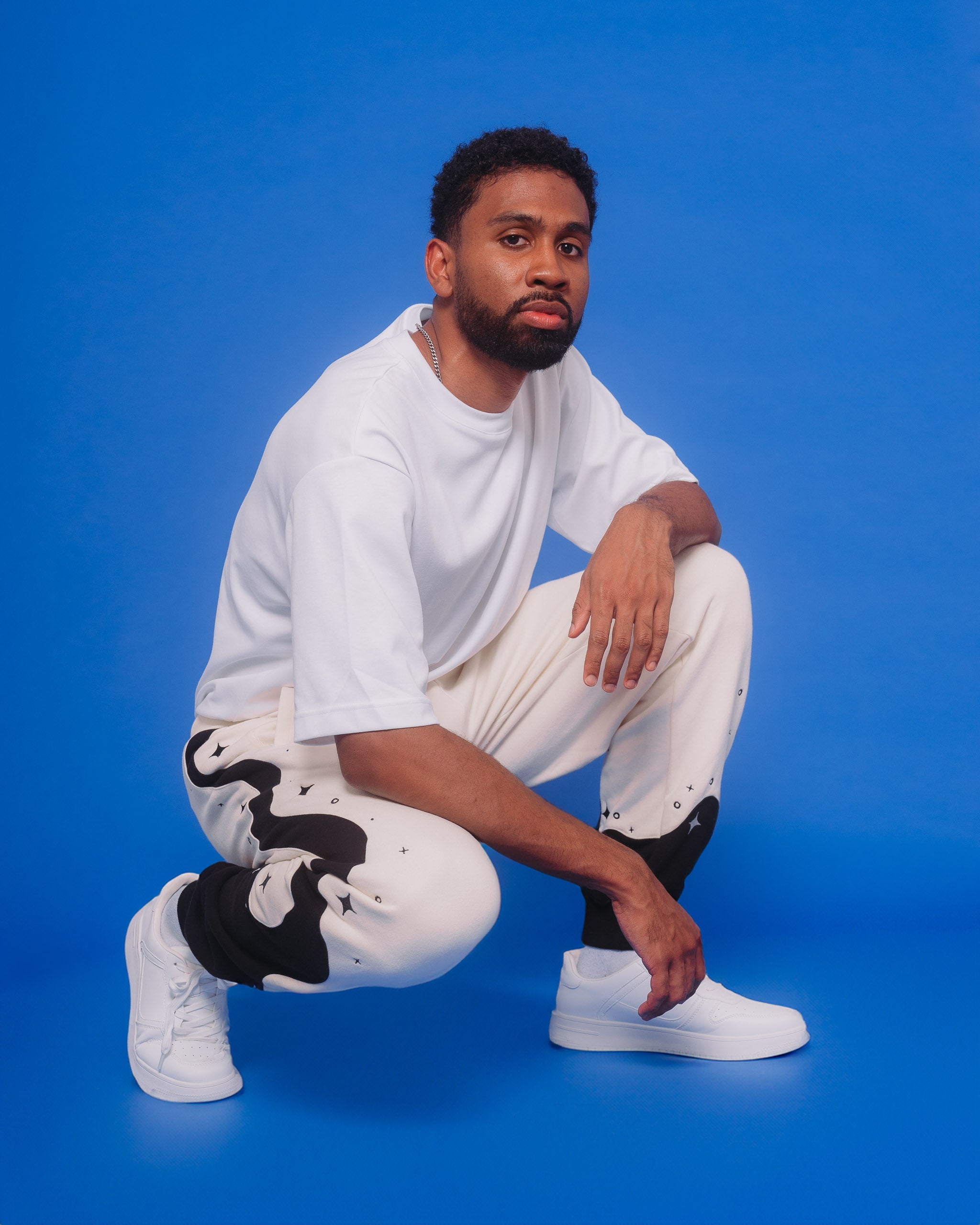 Man wearing supernova joggers in size large kneeling down in front of blue background.