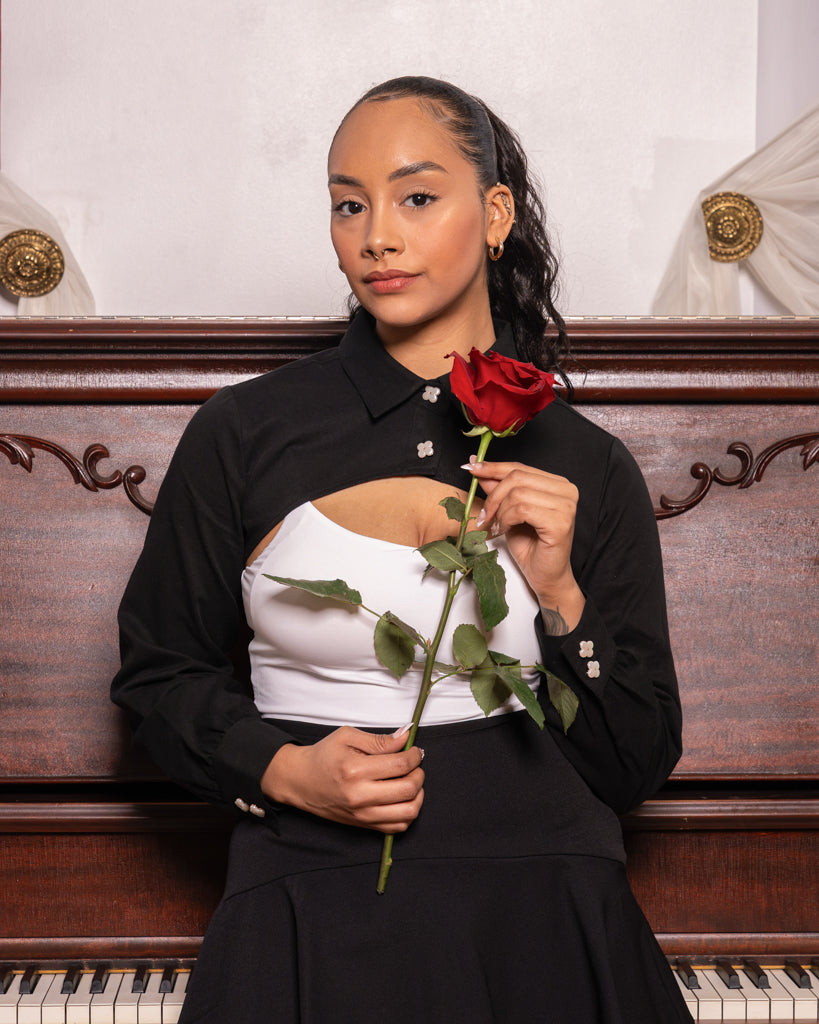Woman wearing black sweetheart bolero shirt in size with white undershirt holding a red rose.
