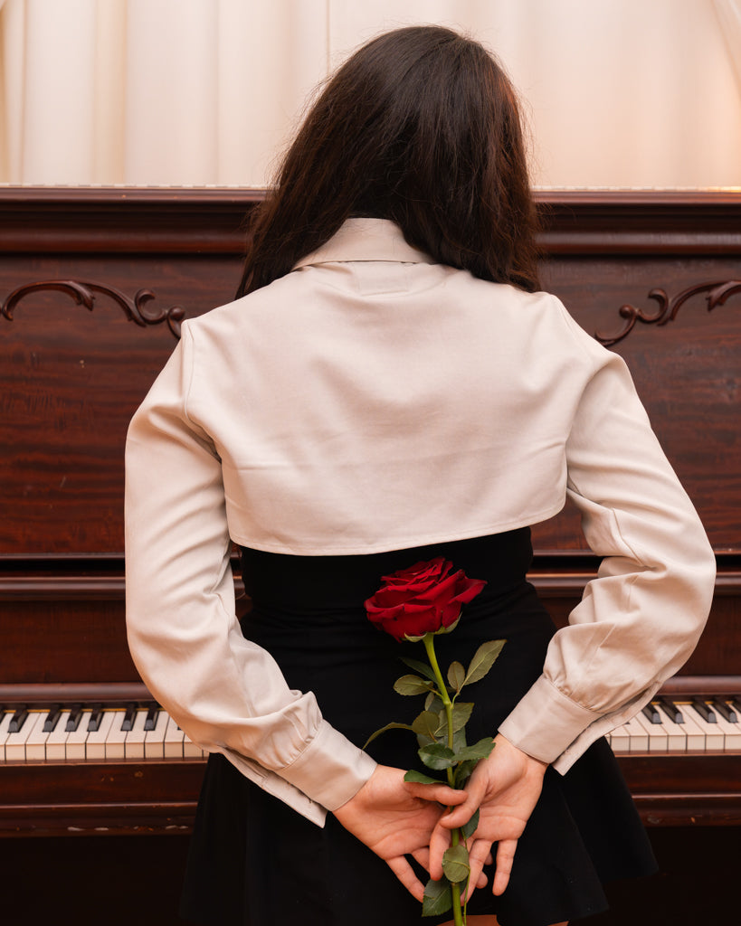 Back view of woman wearing white sweetheart bolero in size small holding a red rose.