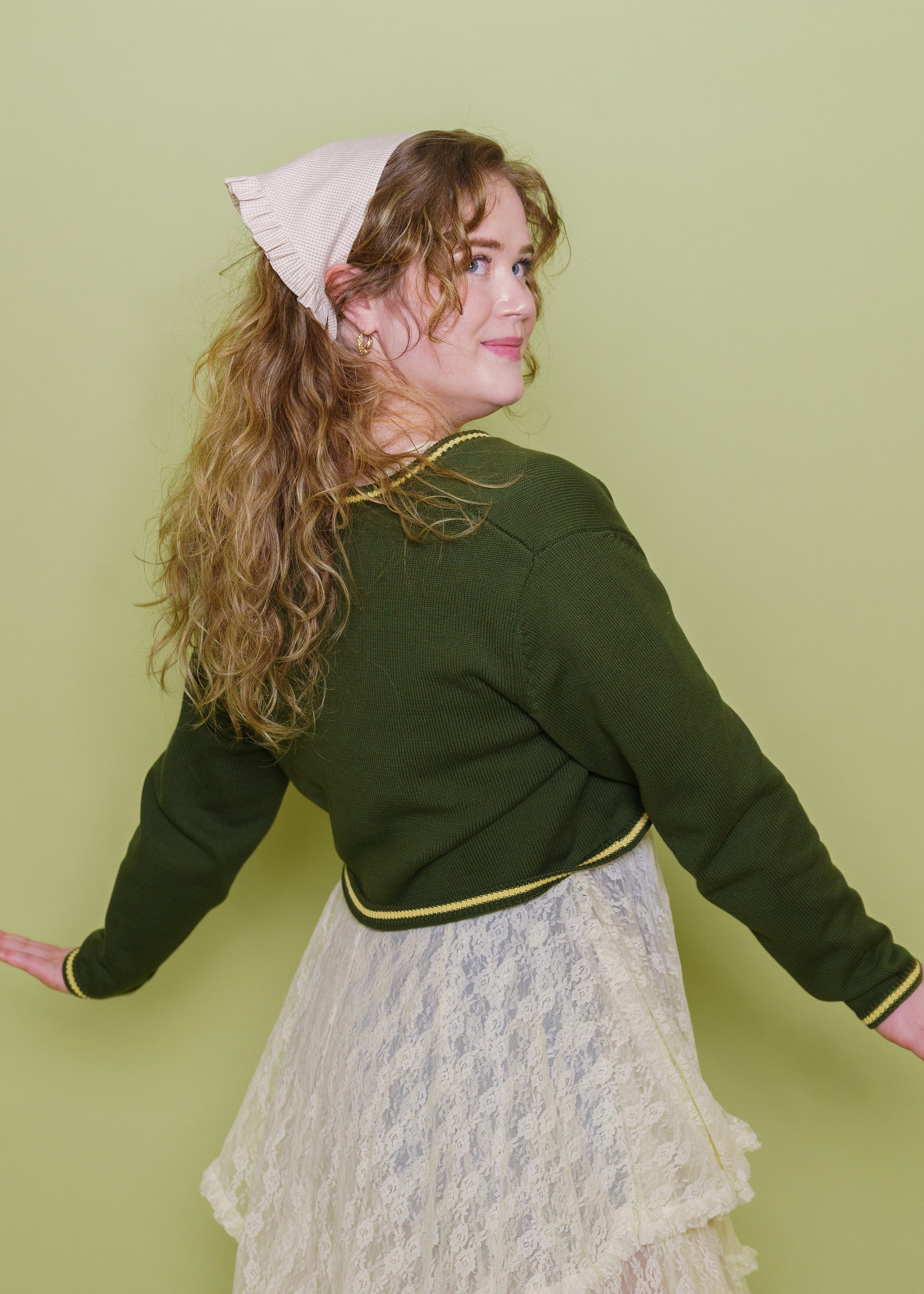 Woman wearing teahouse bandanna in chamomile with herbal cardigan in front of green background.