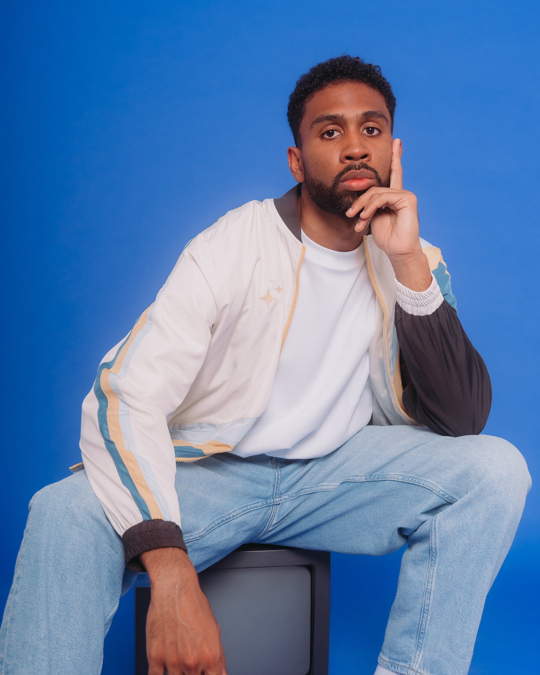 Man wearing under the stars windbreaker in size extra large sitting on old tv in front of blue background.
