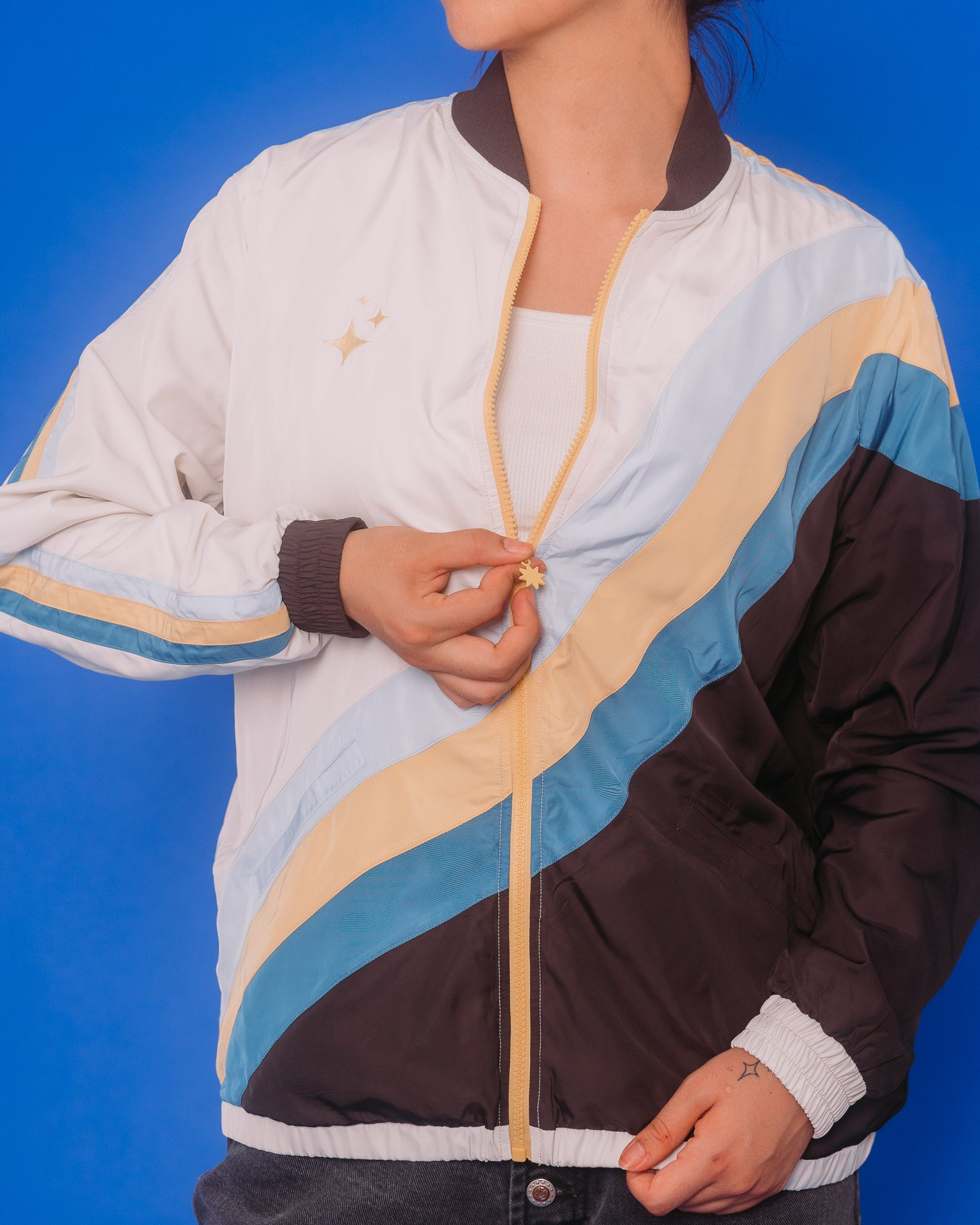 Woman zipping up under the stars windbreaker in size medium in front of blue background.