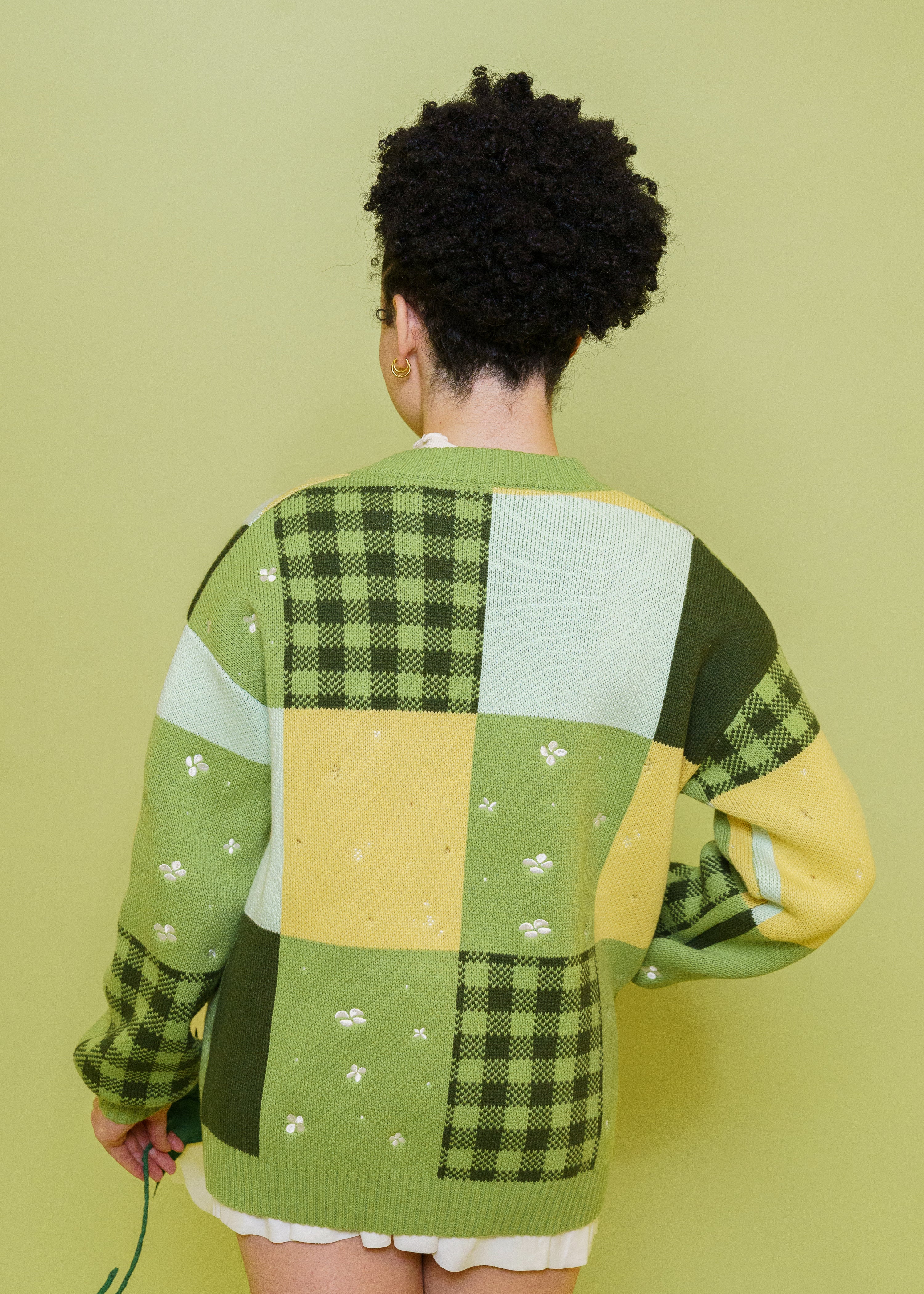 Back view of woman wearing Variety patchwork cardigan in size extra small showing varying patches in front of green background.