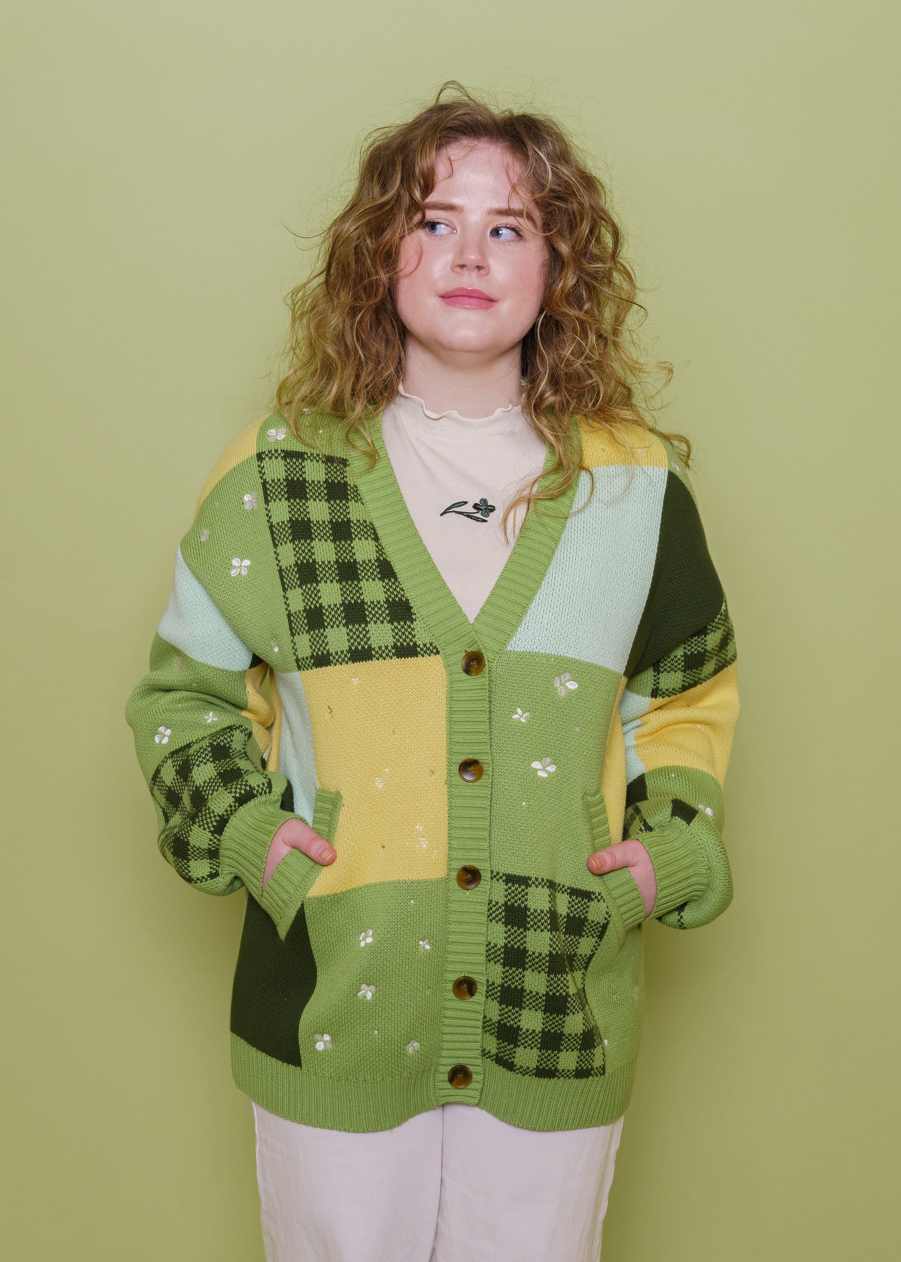 Woman wearing Variety patchwork cardigan in size large buttoned up with hands in pockets in front of green background.