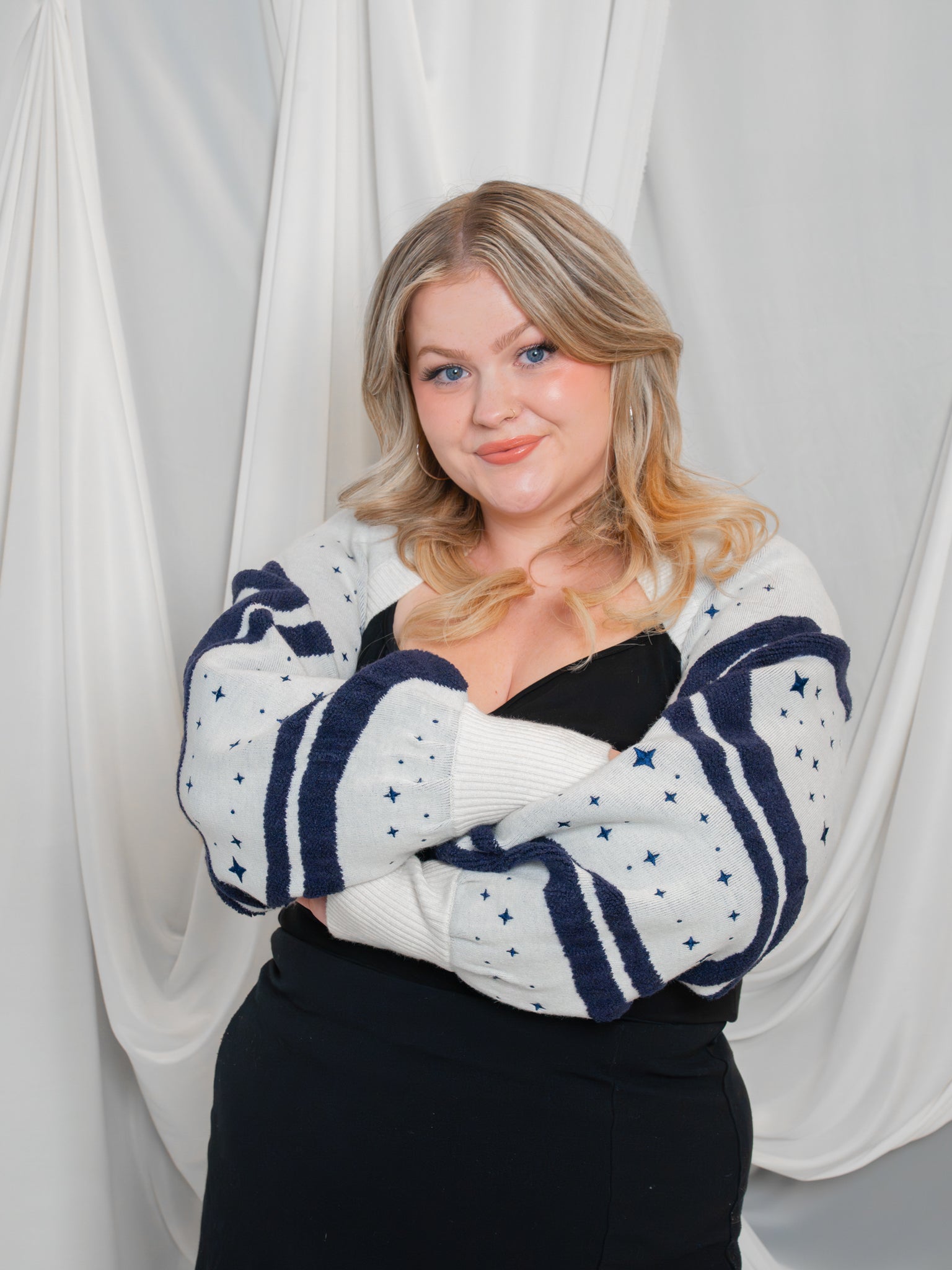 Woman wearing dark blue and white supernova bolero in size large with arms crossed showcasing the wavy design and embroidered sparkle details.