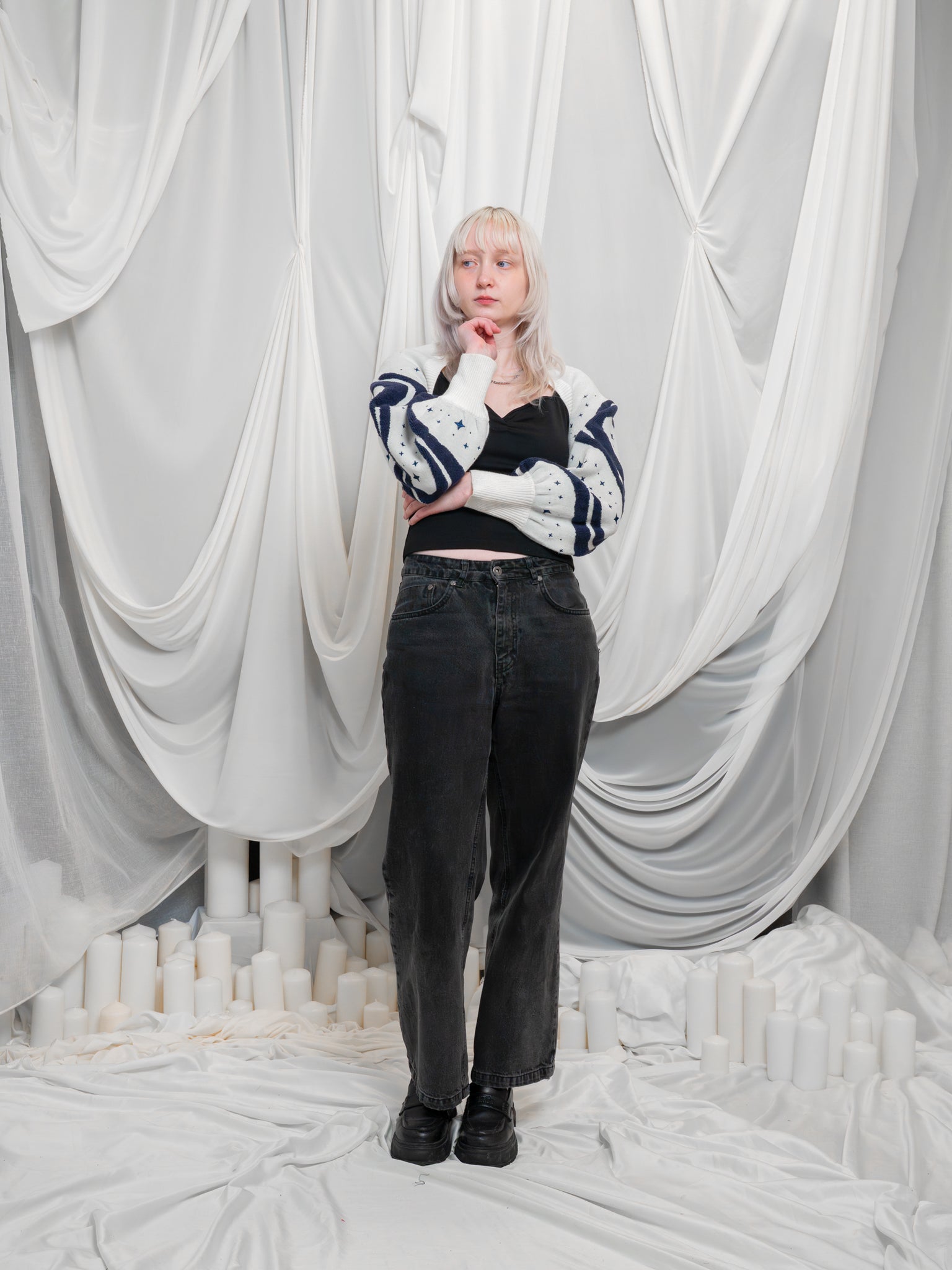 Woman posing wearing dark blue and white supernova bolero in size extra small with black jeans in front of white draped fabric.